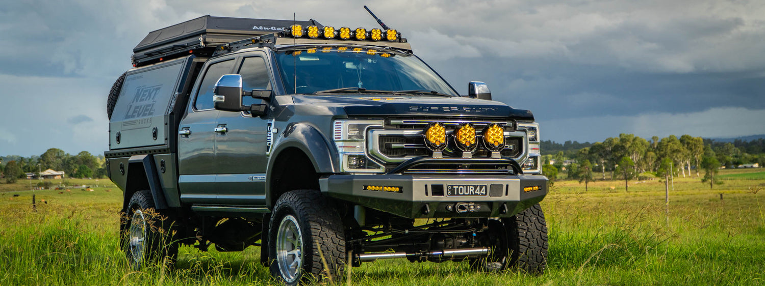 Large pickup truck with off-road equipment in a grassy field under a cloudy sky